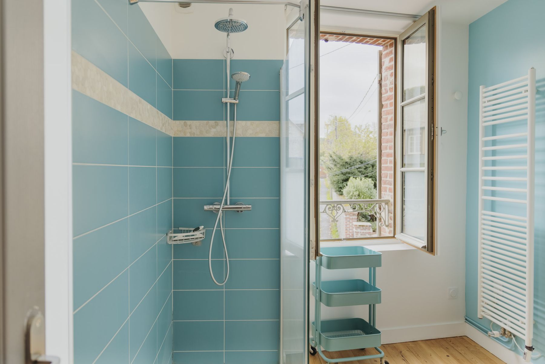 Douche turquoise avec sa fenêtre ouverte sur le jardin