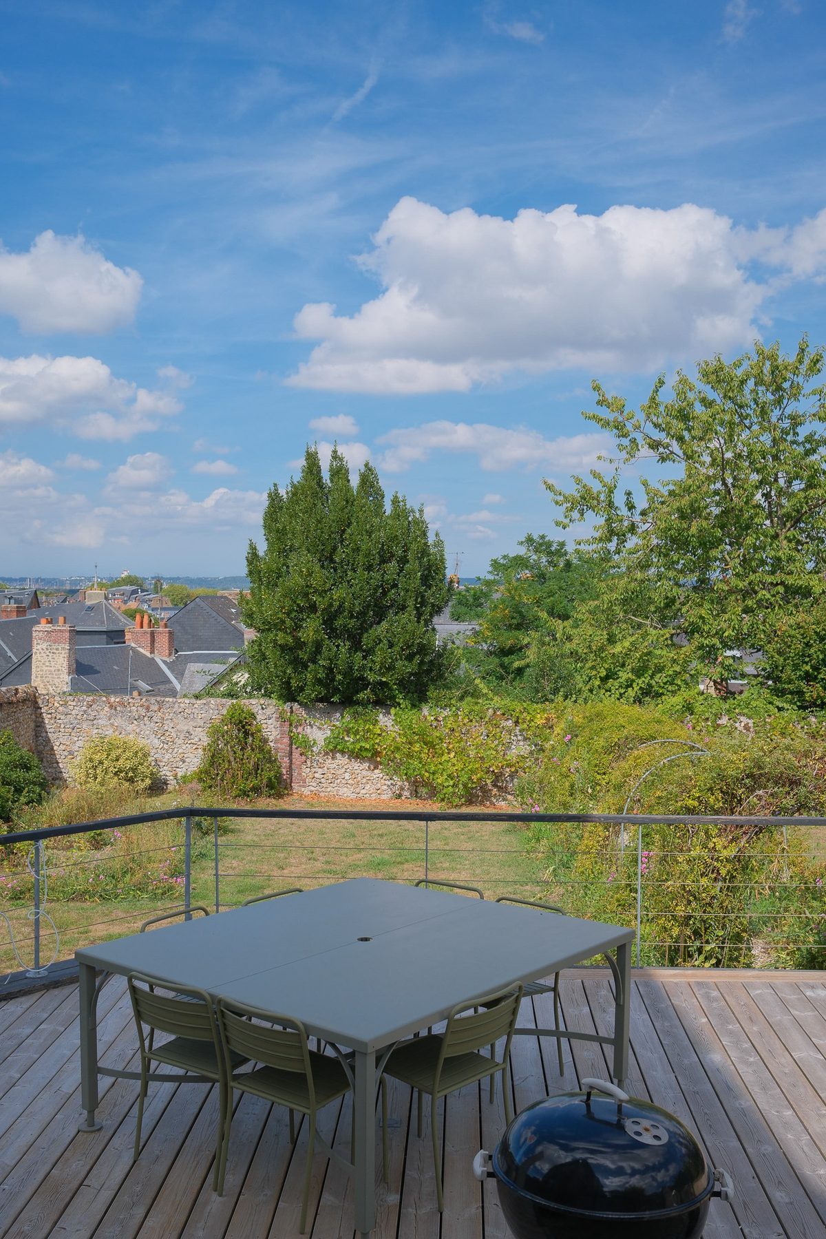 The wooden terrace, its table and the barbecue facing the garden